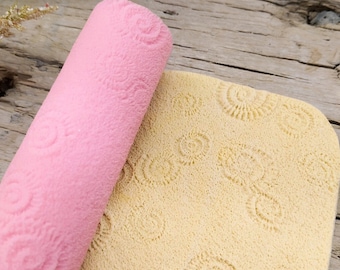 May include: A pink and beige textured fabric with a repeating swirl pattern. The fabric is rolled up and the beige fabric is flat.