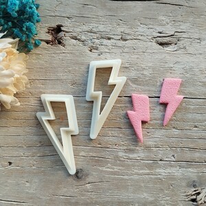 Può includere: Tre stampini per biscotti a forma di fulmini. Due sono di plastica bianca e uno è rosa.