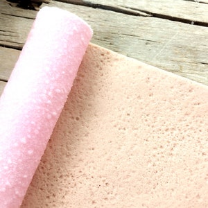 Peut inclure: Un roulé à la crème rose partiellement déroulé sur une surface en bois. Le roulé à la crème est de couleur rose clair et a une surface légèrement texturée.