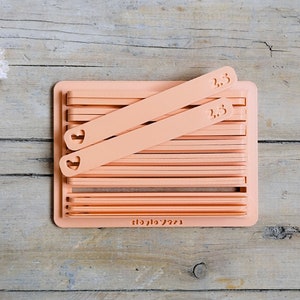 Può includere: Un organizzatore in plastica color pesca con 10 slot per riporre gli articoli per l'artigianato. L'organizzatore ha due slot etichettati "1,5" e due slot etichettati "2,5".