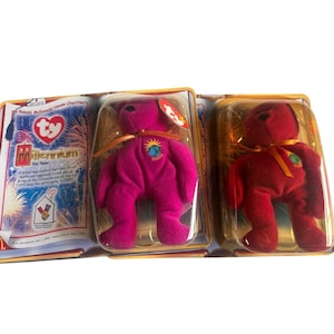 Puede incluir: Dos osos de peluche Beanie Baby en embalaje de plástico. Uno es magenta, el otro rojo oscuro. Ambos tienen una cinta y un parche con un globo terráqueo y el año 2000. El embalaje incluye texto sobre el Milenio.