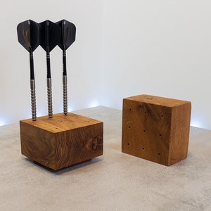 Op de afbeelding: Twee houten blokken met gaten voor darts. Het blok links heeft drie darts erin gestoken. Het blok rechts heeft geen darts. De blokken zijn gemaakt van lichtbruin hout.