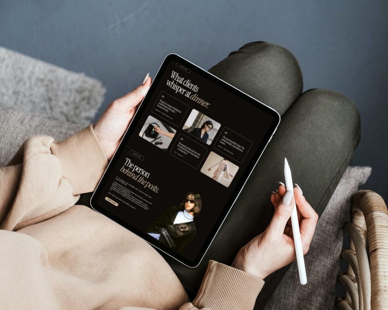 May include: A tablet displaying a dark-themed website with the text What clients whisper at dinner and The person behind the posts. The screen features multiple image thumbnails and a white stylus is held in the hand next to the device.