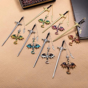 K&ouml;nnte beinhalten: Eine Sammlung von Fantasy-Lesezeichen mit schwertf&ouml;rmigen Designs und Drachenanh&auml;ngern. Die Drachen sind in verschiedenen Farben wie Gr&uuml;n, Blau, Rot und Lila gehalten und weisen aufwendige Details auf. Jedes Lesezeichen hat eine Kette und ein Namensschild.