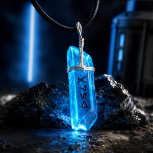 Op de afbeelding: Een helderblauwe kristallen hanger met zilverkleurig draad en een zwart koord. De kristal heeft gegraveerde symbolen en staat tegen een donkere, getextureerde achtergrond. Een uniek sieraad.