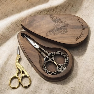 Peut inclure: Une boîte en bois avec un motif de papillon gravé sur le couvercle. La boîte est ouverte et contient une paire de ciseaux dorés avec un motif floral. La boîte est étiquetée "Mary's Scissors".