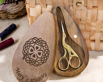 May include: A wooden box with a Celtic knot design and the words "Mary's scissors" engraved on the front. The box is open and a pair of gold-colored bird-shaped scissors are inside.