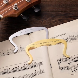 Könnte beinhalten: Zwei silberne und goldene Lesezeichen mit eingravierten inspirierenden Zitaten. Das silberne Lesezeichen sagt "faith over fear" und das goldene Lesezeichen sagt "when words fade, music speaks".