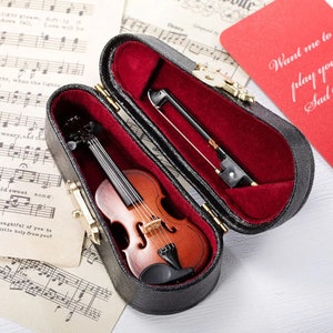 May include: A miniature violin and bow in a black velvet case with red lining. The case is open and the violin is visible inside. The case has a brass latch.