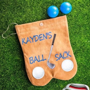 May include: A brown golf ball sack with the name "KAYDEN'S BALL SACK" printed on it. The sack has a golf club and golf balls printed on it.