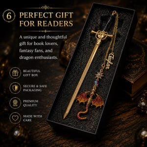 K&ouml;nnte beinhalten: Ein goldfarbener, schwertf&ouml;rmiger Lesezeichen mit schwarzem Griff und Drachenanh&auml;nger. Das Lesezeichen befindet sich in einer schwarzen Geschenkbox. Der Text auf dem Bild lautet "PERFECT GIFT FOR READERS".