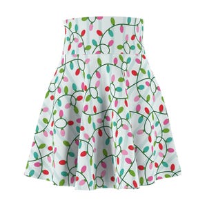 Puede incluir: Falda skater blanca con un estampado repetido de luces navideñas de colores. Las luces son rojas, verdes, rosas y turquesas, conectadas por cables verdes, sobre un fondo a rayas azul claro. La falda tiene cintura alta.