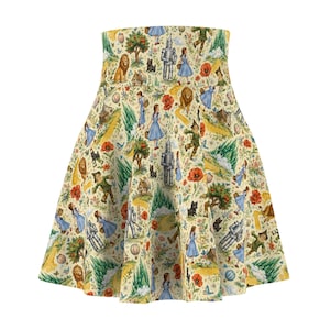May include: A high-waisted skater skirt featuring a repeating pattern of characters and scenes from The Wizard of Oz, including Dorothy in a blue dress, the Tin Man, the Scarecrow, the Cowardly Lion, and Toto, set against a cream-colored background.