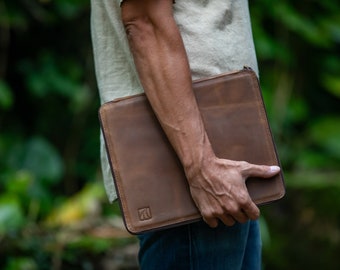 May include: A brown leather laptop sleeve with a zipper closure. The sleeve has a small logo on the front.
