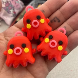 Puede incluir: Tres abalorios rojos en forma de pulpo con detalles en rosa y amarillo. Cada abalorio tiene un ojo negro y una boca rosa.