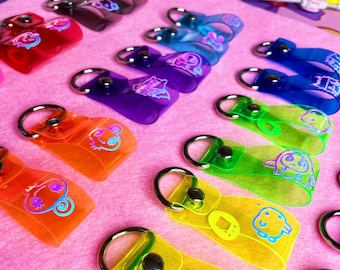 May include: A collection of colorful, transparent keychains with different cartoon characters printed on them. The keychains are made of plastic and have a silver metal ring.