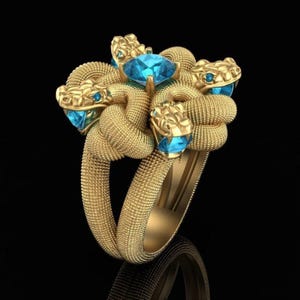Peut inclure: Une bague en or au design de serpent enroulé et texturé, avec quatre têtes de serpent entourant une pierre précieuse centrale bleu vif à facettes. Chaque tête de serpent a de petits yeux bleus et l'anneau présente une texture granuleuse.