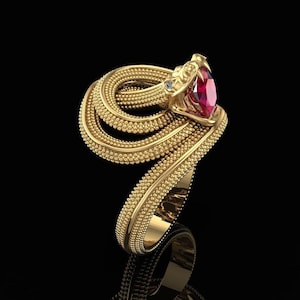 May include: A gold-coloured ring shaped like a snake, featuring a large, oval-cut red gemstone. The snake's head is intricately detailed, and the body coils around the finger. A small, clear gemstone is set on the snake's head.