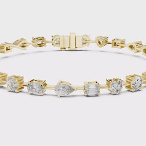 May include: A gold bracelet featuring a series of diamonds in various shapes, including round, oval, and emerald cuts. The bracelet is secured with a clasp and is set against a white background.