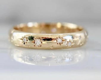 Op de afbeelding: Een goudkleurige ring met een hemels ontwerp. De ring heeft ingebedde stervormige accenten met kleine, heldere edelstenen. De band is glad en gepolijst en reflecteert licht. De ring is een sieraad.
