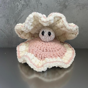 May include: A crocheted pink and white clam with black eyes. The clam is closed and has a ruffled edge.