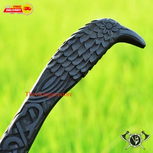 Könnte beinhalten: Nahaufnahme einer schwarzen Holzschnitzerei eines Rabenkopfes. Die Schnitzerei ist detailliert und kunstvoll, mit Federn und einem Blumendesign auf dem Kopf. Die Schnitzerei ist Teil eines größeren Stücks, wahrscheinlich eines Spazierstocks oder eines Stabes.