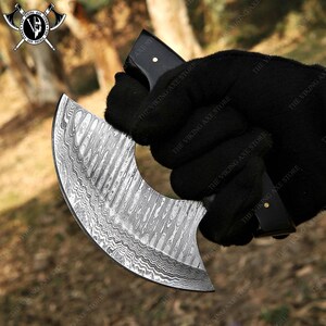 May include: A black handled knife with a curved, silver blade featuring a Damascus steel pattern. The blade is about 7 inches long.