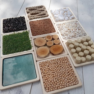 Op de afbeelding: Een set van 10 houten zintuiglijke bakken met verschillende texturen en materialen. De bakken zijn in een rasterpatroon gerangschikt en bevatten items zoals touw, bonen, kikkererwten, hout en gras.