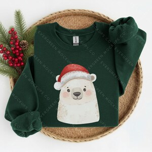 May include: A dark green long-sleeve sweatshirt featuring a graphic of a white polar bear wearing a red and white Santa hat. The sweatshirt has a crew neckline and is displayed with a sprig of green pine needles and red berries.