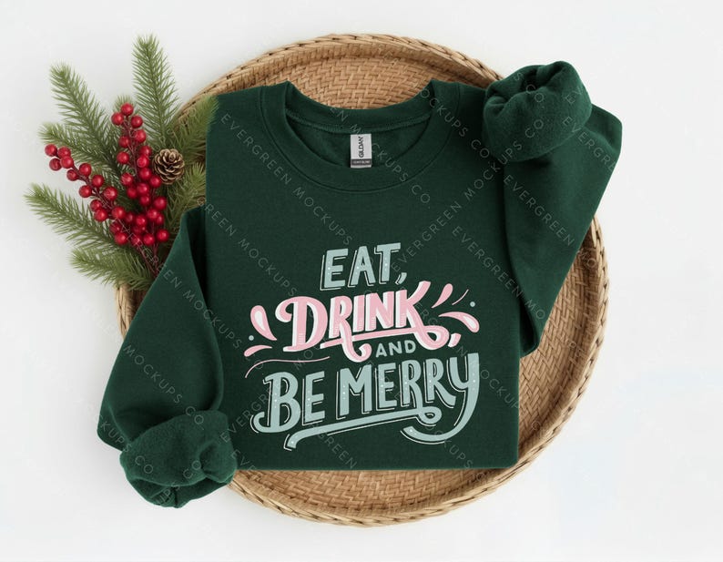 May include: A dark green long-sleeve sweatshirt featuring the text EAT, DRINK AND BE MERRY in a stylised font. The word DRINK is in light pink, while EAT, AND, and BE MERRY are in a light teal colour. The garment has a crew neckline.
