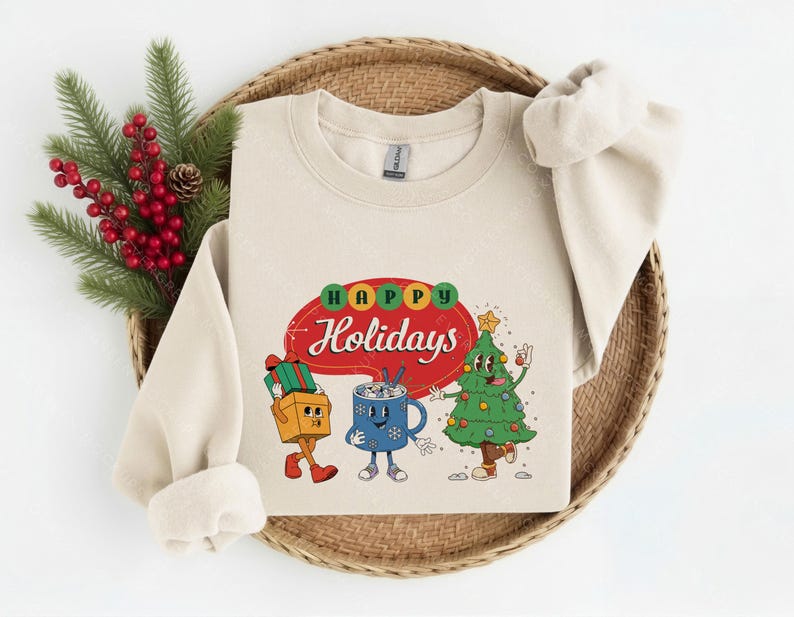 May include: A beige crewneck sweatshirt featuring a graphic print with the text Happy Holidays in a red speech bubble. The design includes a cartoon gift box, a blue mug with a face, and a decorated Christmas tree with arms and legs.