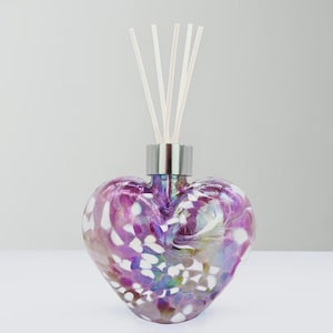 Peut inclure: Un diffuseur en verre en forme de cœur avec un col argenté et des bâtonnets blancs. La bouteille est un mélange de couleurs violettes, blanches et irisées. Le diffuseur est conçu pour libérer du parfum dans l'air.