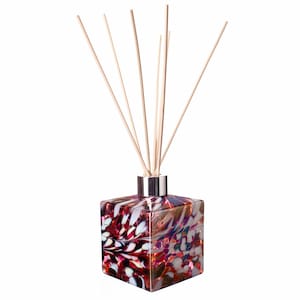 May include: A square glass diffuser bottle with a red, white and gold swirl pattern. The bottle has a silver cap and wooden sticks sticking out of the top.