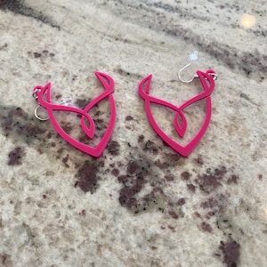 Può includere: Un paio di orecchini pendenti rosa con un design astratto unico. Gli orecchini sono realizzati in un materiale leggero e hanno un aspetto semplice e moderno.
