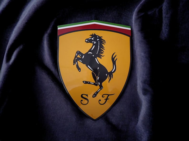 May include: A yellow shield with a black rearing horse and the letters "S F" in a stylized font. The shield has a red, white, and green stripe across the top.