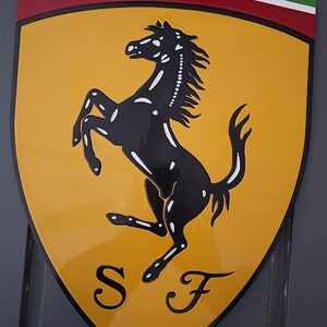 May include: A yellow shield-shaped sign with a black rearing horse and the letters "SF" in black. The shield has a red, white, and green stripe at the top.