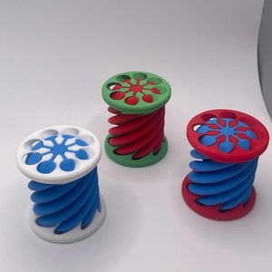 以下が含まれることがあります： 3Dプリントされた、多色のらせん状のオブジェクトが3つあります。オブジェクトはプラスチック製で、上部と下部に星形のデザインが施されています。オブジェクトは赤、緑、青です。