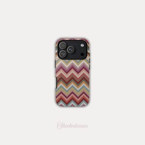 May include: A smartphone case featuring a zig-zag pattern in red, pink, yellow, and blue. The case has a black camera module and the text "Stackedeases" in a cursive font.