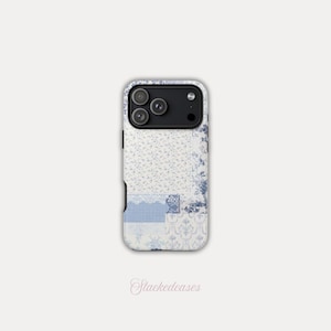 May include: A phone case with a patchwork design featuring floral patterns, lace, and gingham in shades of blue and white. The case has a black camera module and the text "Stackedeases" in a script font.