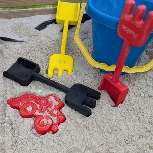 Pode incluir: Um conjunto de quatro brinquedos de pl&aacute;stico coloridos para crian&ccedil;as para brincar numa caixa de areia. O conjunto inclui uma p&aacute; amarela, uma p&aacute; vermelha, uma p&aacute; preta e um balde azul.