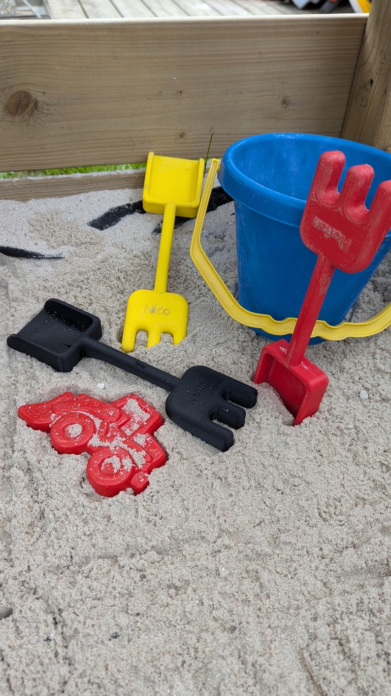 Pode incluir: Um conjunto de quatro brinquedos de pl&aacute;stico coloridos para crian&ccedil;as para brincar numa caixa de areia. O conjunto inclui uma p&aacute; amarela, uma p&aacute; vermelha, uma p&aacute; preta e um balde azul.