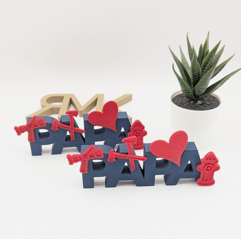 K&ouml;nnte beinhalten: Zwei blaue Holzschilder, die "PAPA" buchstabieren, mit roten Herzen und Feuerwehrhydranten-Akzenten. Die Schilder stehen auf einer wei&szlig;en Oberfl&auml;che.
