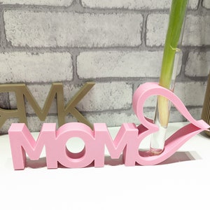 Pu&ograve; includere: Vaso rosa MOM con un'apertura a forma di cuore per un solo fiore. Il vaso &egrave; in plastica e ha un tubo di vetro trasparente per contenere l'acqua.