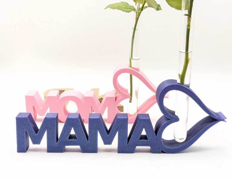 Pu&ograve; includere: Un cartello in legno blu che scrive "MAMA" con due vasi di fiori a forma di cuore rosa e blu con provette di vetro trasparente per contenere i fiori.