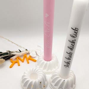 Peut inclure: Deux bougeoirs blancs avec une bougie rose et blanche. Les bougies portent l'inscription "Ich hab dich lieb" et "Ich lieb dich".