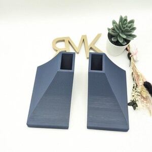 Puede incluir: Dos soportes de estante triangulares de color azul oscuro, impresos en 3D, con un recorte cuadrado en el centro.