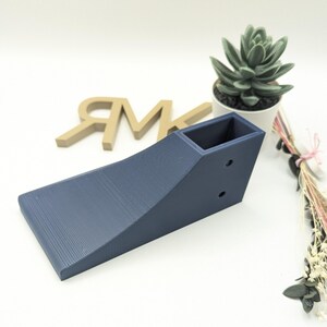 Puede incluir: Una rampa de color azul oscuro impresa en 3D con una peque&ntilde;a abertura rectangular en la parte superior. La rampa est&aacute; dise&ntilde;ada para usarse con coches de juguete u otros objetos peque&ntilde;os.