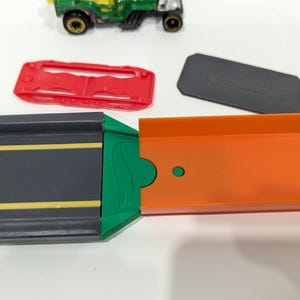 Peut inclure: Un ensemble de circuit de course pour jouets vert, orange et noir avec une voiture verte et noire sur le circuit.