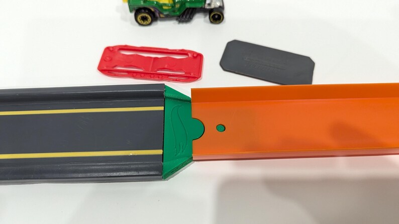 Peut inclure: Un ensemble de circuit de course pour jouets vert, orange et noir avec une voiture verte et noire sur le circuit.