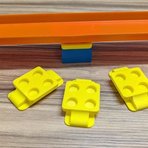 Peut inclure: Trois pi&egrave;ces de piste en plastique jaune avec six trous chacune, con&ccedil;ues pour un ensemble de piste de course pour enfants. Les pi&egrave;ces sont sur une surface en bois, avec une pi&egrave;ce de piste orange vif.